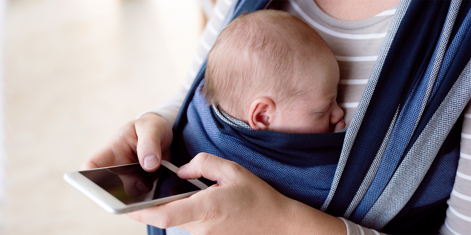 Kvinde med nyfødt barn i bæresele holder en mobiltelefon